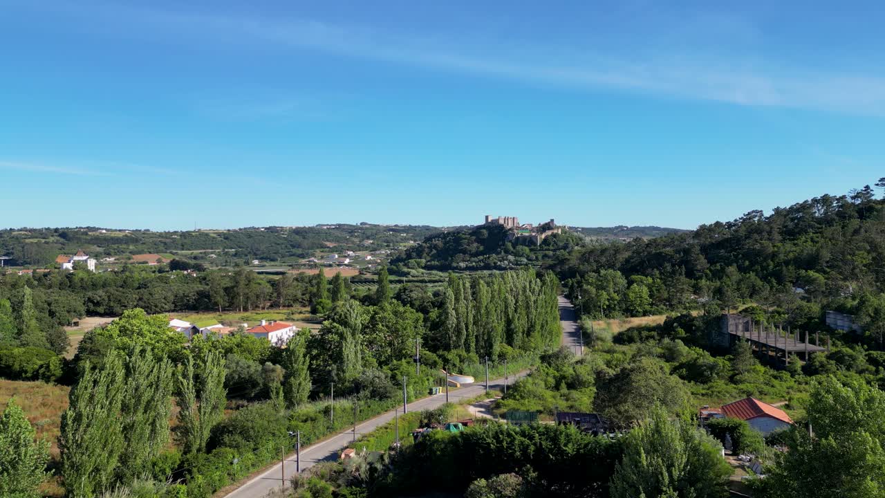 Aerial view of a scenic landscape in Portugal during the daytime, showcasing a winding road, lush greenery, and a distant castle. The serene countryside captures the essence of rural beauty.