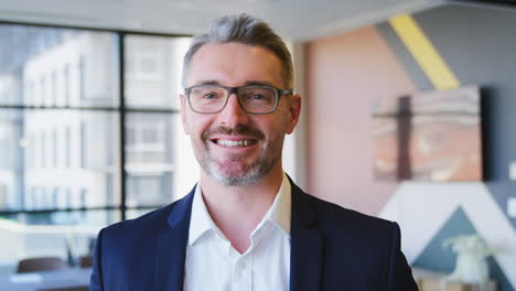 Portrait-Of-Smiling-Mature-Businessman-Wearing-Glasses--Standing-In-Empty-Office