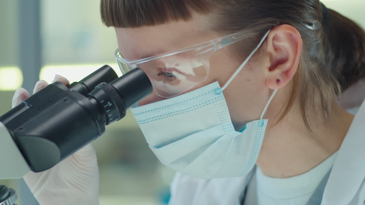 Female Lab Scientist in Mask Using Microscope