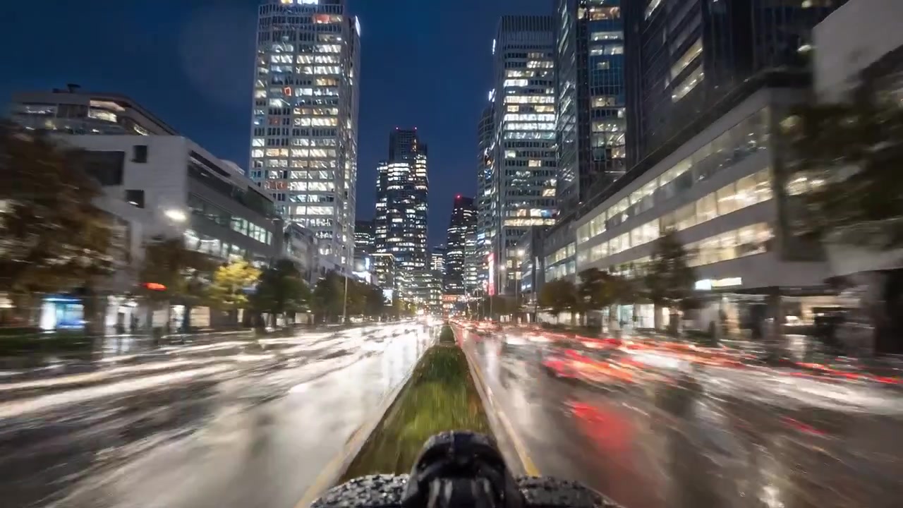 A Scenic Night Drive Through a Bustling Urban Cityscape with Reflections and Bright Lights Amidst Rainy Weather Captured in Dynamic Motion