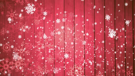 animation of snow falling on red wooden background with copy space at christmas