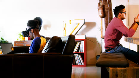 Gay-couple-using-virtual-reality-headset,-laptop-and-digital-tablet-in-living-room