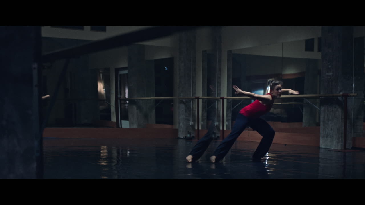 A young woman practices modern dancing and ballet in a moody room full of mirrors