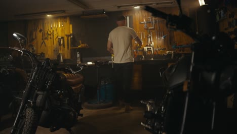 blond guy in a white t-shirt mechanic works and repairs a motorcycle in his workshop