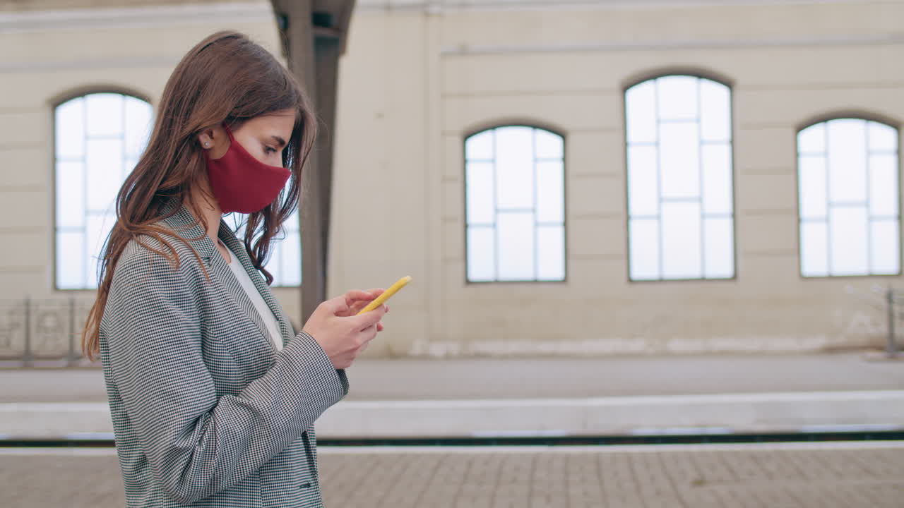 Woman in face mask using smartphone at a train station