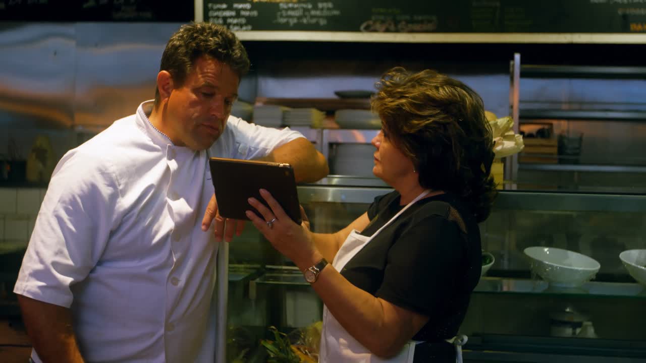cocineros discutiendo sobre una tableta digital en la cocina comercial 4k