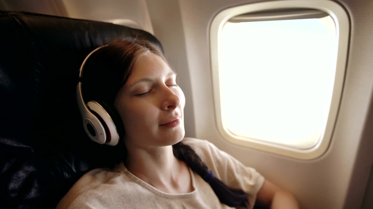joven con auriculares inalámbricos escuchando música y sonriendo durante un vuelo en avión