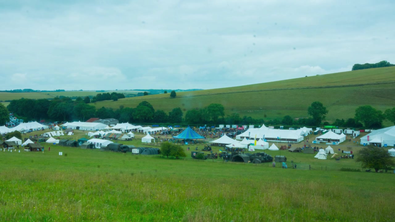 Timelapse di tende da festival, tendoni e veicoli militari ambientato in una verde valle del Wiltshire.