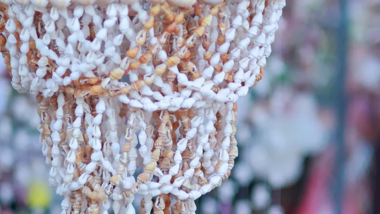 A person's hand gently touches a handcrafted seashell chandelier at a market in Thailand