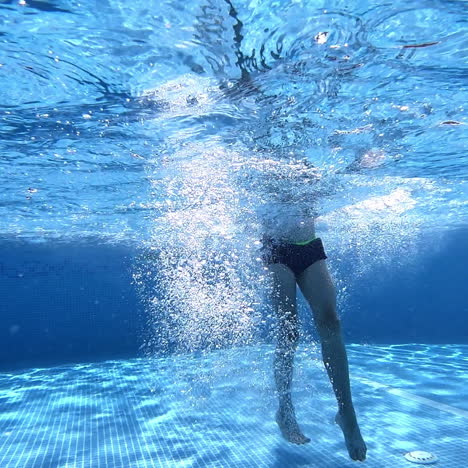 Boy swimming under the clear water in the swimming pool. Young guy jumps underwater and swims with closed eyes and nose on a blue background. Underwater video.