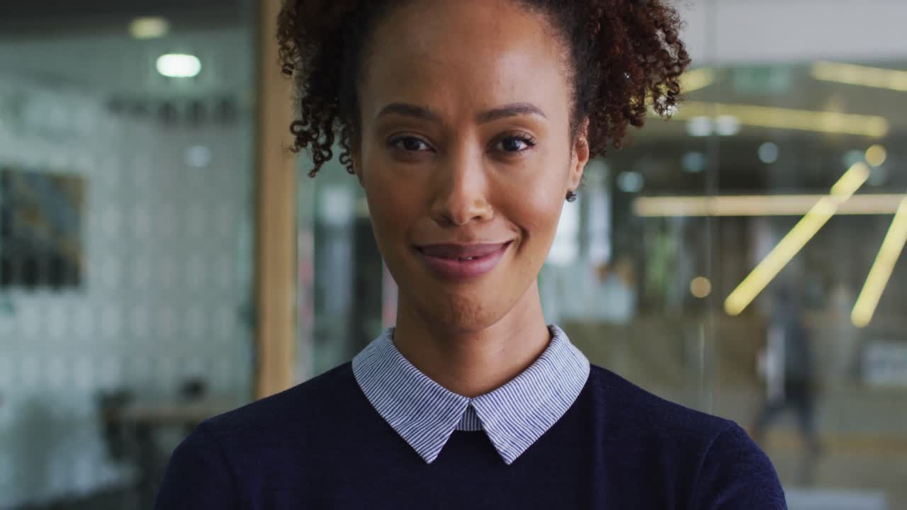 Portrait of smiling mixed race businesswoman in blue jumper standing in office