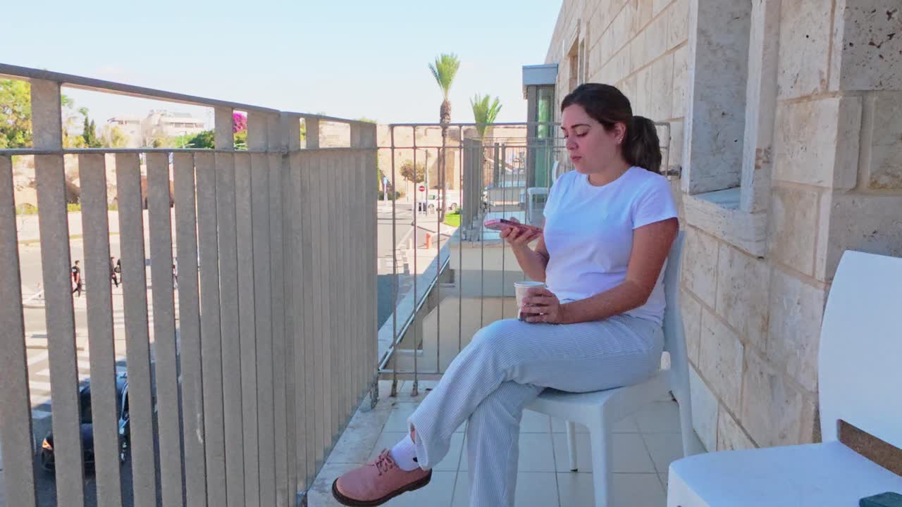 Donna che usa l'app del telefono su un balcone con vista su una città storica