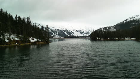 Luftaufnahme-Tief-über-Dem-Meer,-Inmitten-Der-Schneebedeckten-Berge-Der-Cloudy-Bettles-Bay,-Alaska