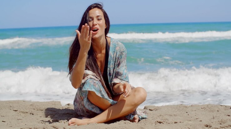 ein hübsches mädchen sitzt auf dem sand am strand und küsst ihre handfläche