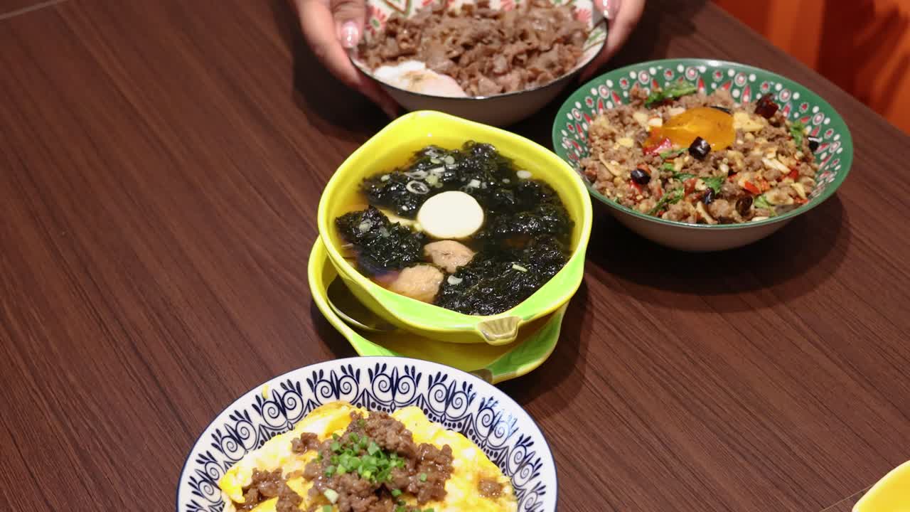 Multiple vibrant rice meals, including Thai cuisine, are gradually removed from a wooden table under bright indoor lighting, captured from a top-down perspective