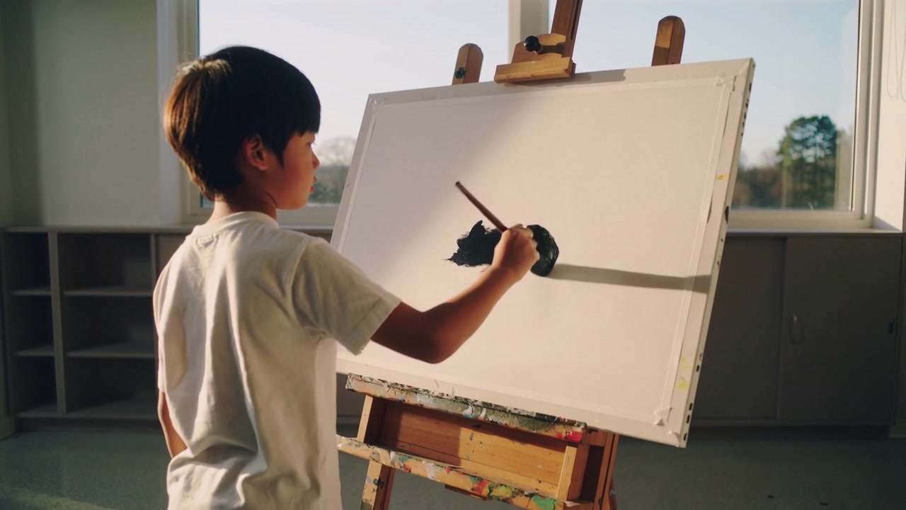 絵を描く少年が、地平線を示す細い線を描き、筆に絵の具をつけ、スタジオのイーゼルに暗い部分を作っている。
