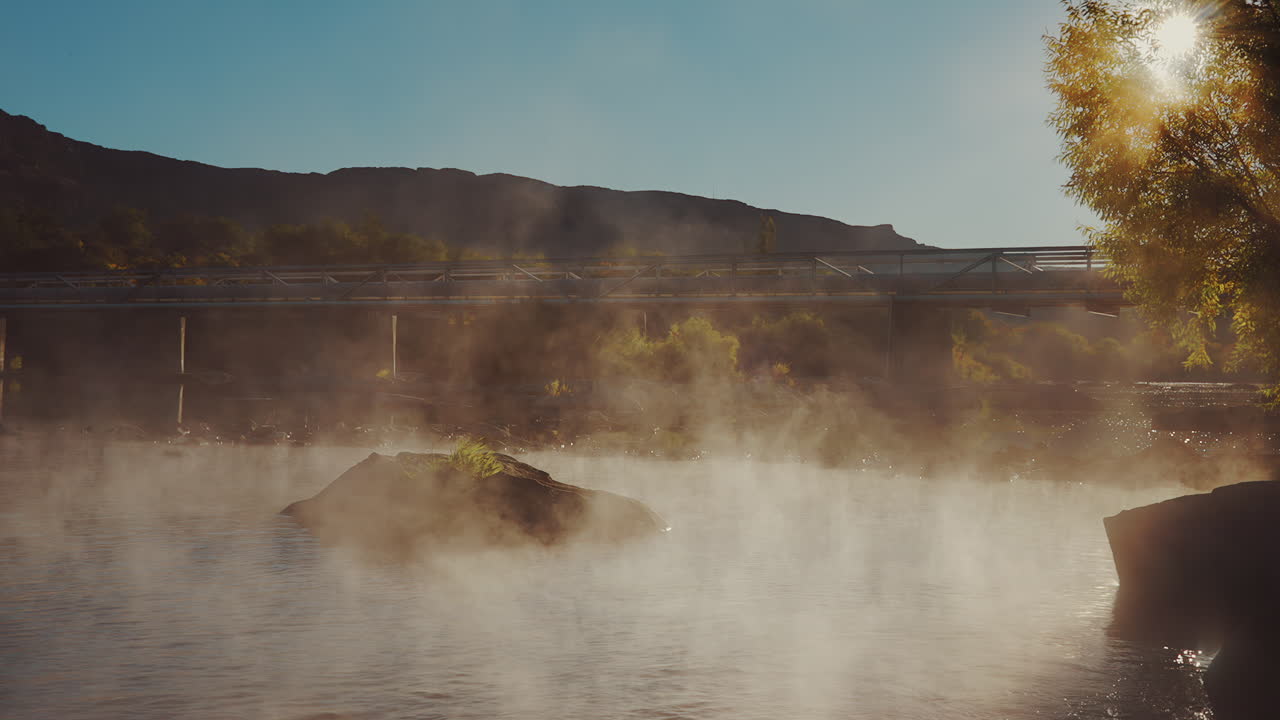 niebla que se levanta sobre un río tranquilo con puente y montaña en el fondo