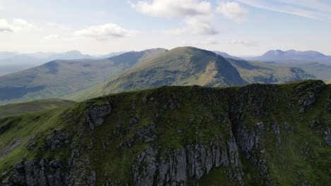 a male standing on the top of green mountain ridge fannichs between the peaks of the scottish highlands on a sunny day