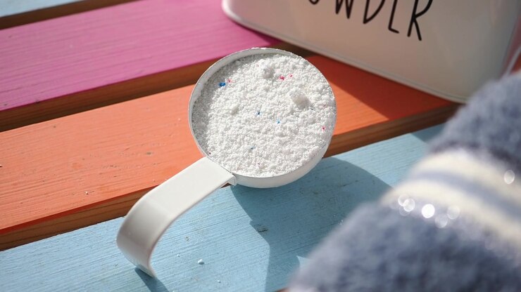 Measuring Scoop Filled with Laundry Detergent Powder on Colorful Wooden Surface