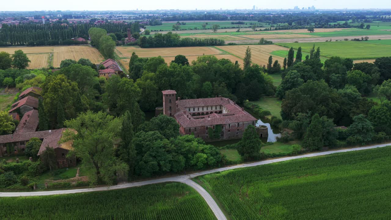 Castello Borromeo surrounded by moat, lush trees, and green agricultural fields in Italian countryside, Peschiera Borromeo, Italy. Aerial drone