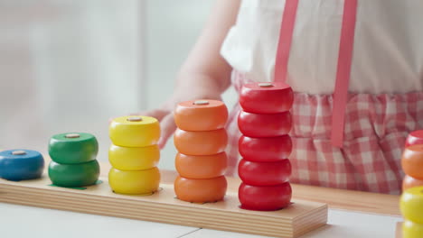 niña de 3 años aprendiendo colores y números mientras juega apilando anillos coloridos de madera y ordenando por colores en columnas