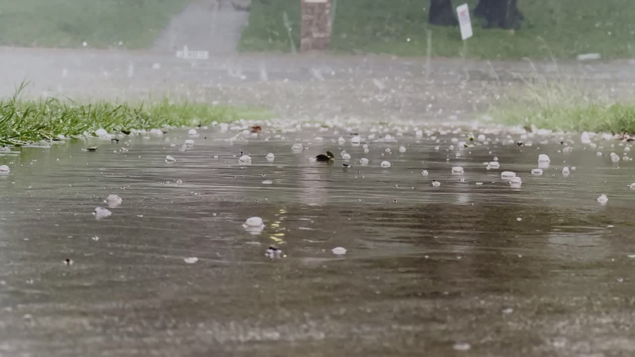Hailstones and heavy rain create a dramatic scene on a wet paved surface. The severe weather showcases the powerful impact of nature's elements during a storm