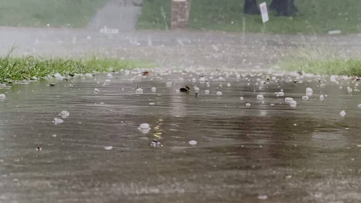 Hailstones and heavy rain create a dramatic scene on a wet paved surface. The severe weather showcases the powerful impact of nature's elements during a storm