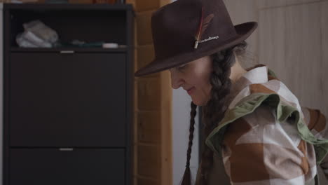 home maker walking into room, shutting door behind her with focused expression, strides firm on rustic tiled floor, braids swaying under hat brim, sidelights casting soft shadows under winter light