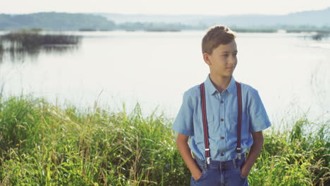 portrait of the cute small teen boy standing on the big lake shore and looking at the camera