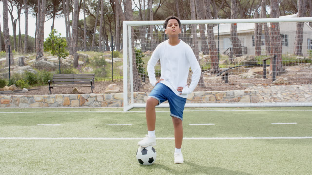 Confident boy standing on soccer field with foot on ball, ready to play, copy space