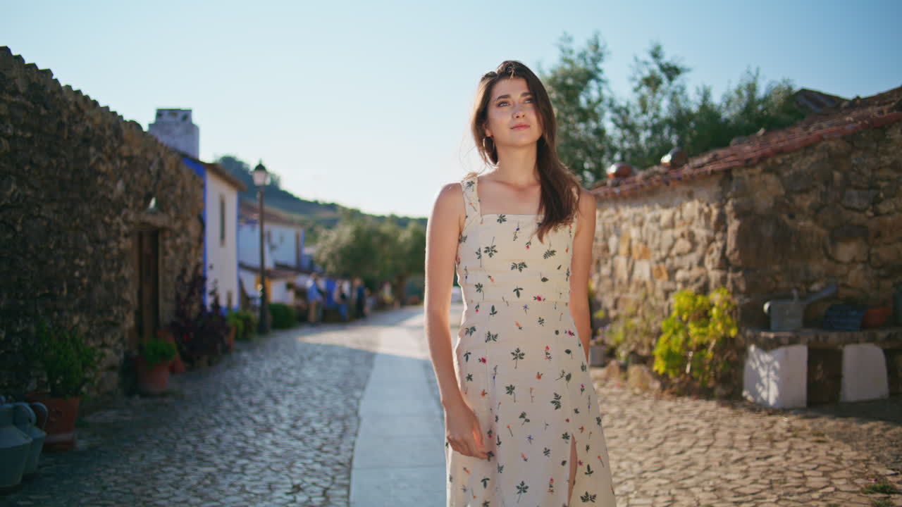 modelo relajado paseando por un callejón soleado pavimentando piedras. mujer caminando por el pueblo