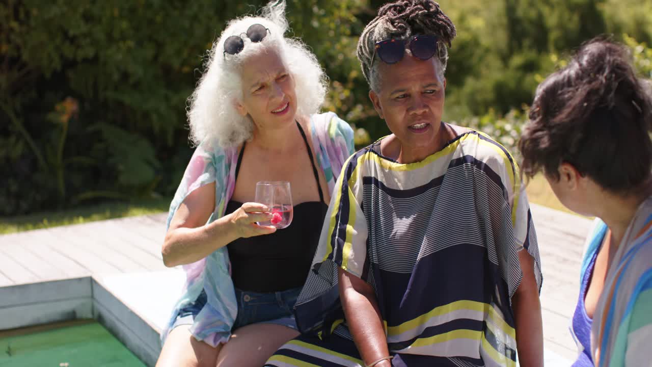 Turning African American woman starting chat with friends in coverups on pool deck with pink drinks