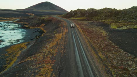 white land rover driving down lonely road in colorful volcanic landscape during adventure travel road trip