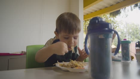 an adorable boy enjoys eating spaghetti in a cafeteria, with a cute and playful expression, capturing a fun and heartwarming mealtime moment