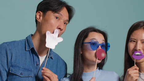 Group-Of-Young-Friends-In-Front-Of-Blue-Studio-Background-Having-Fun-Posing-For-Photo-Booth-Style-Portraits-With-Props-2