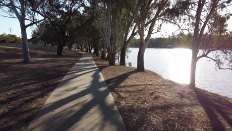 Drone-flying-over-a-walking-path-at-low-altitude-near-a-river-parkland