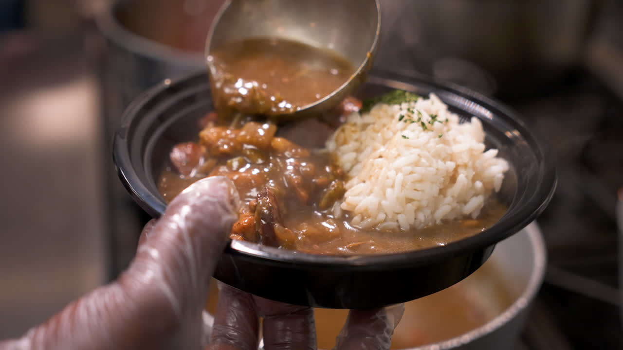 Cook ladles dark rich steaming gumbo into bowl over white rice, slow motion close up 4K