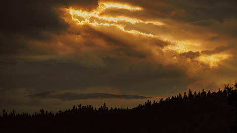 Timelapse-close-up-shot-showing-orange-sun-rays-piercing-through-the-clouds,-illuminating-the-silhouettes-of-distant-mountains,-high-contrast