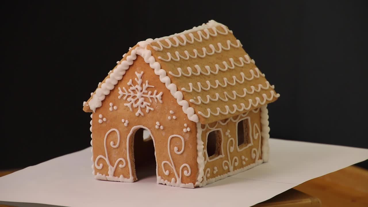 Homemade gingerbread house rotating in the studio. Christmas gingerbread cookies. Little gingerbread house with royal icing glaze. Christmas house from ginger cookies. Christmas sweets and gifts.