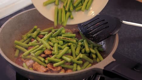 sauteing pork meat and beans on a frying pan with a black flat holed ladle, combining flavors - close up