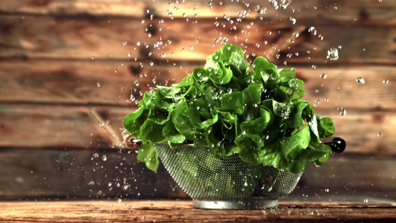 Gocce d'acqua che cadono su lattuga verde fresca in uno scolapasta