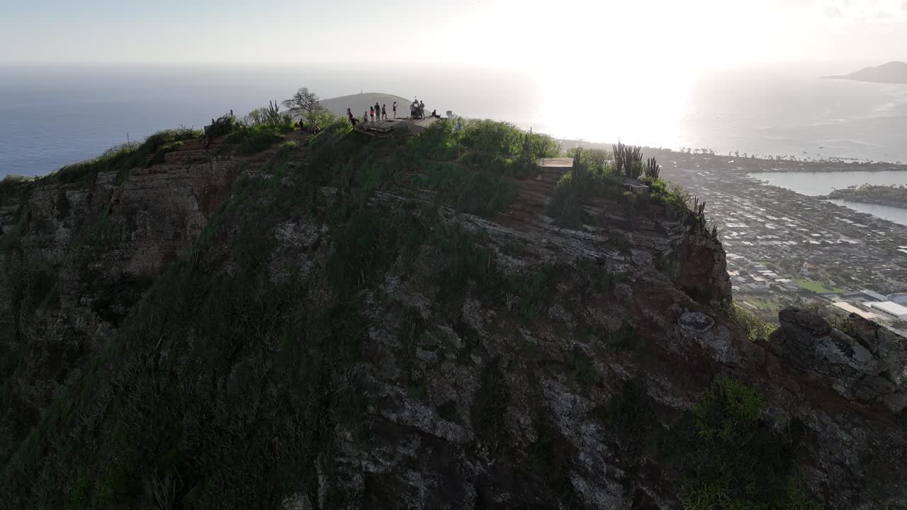 60fps 슬로우 모션 드론으로 하나우마 베이가 전경에 있는 등산객과 함께 코코 헤드 산을 넘어가고 하이킹 코스와 이웃을 보여주는 아름다운 푸른 바다를 보여줍니다.