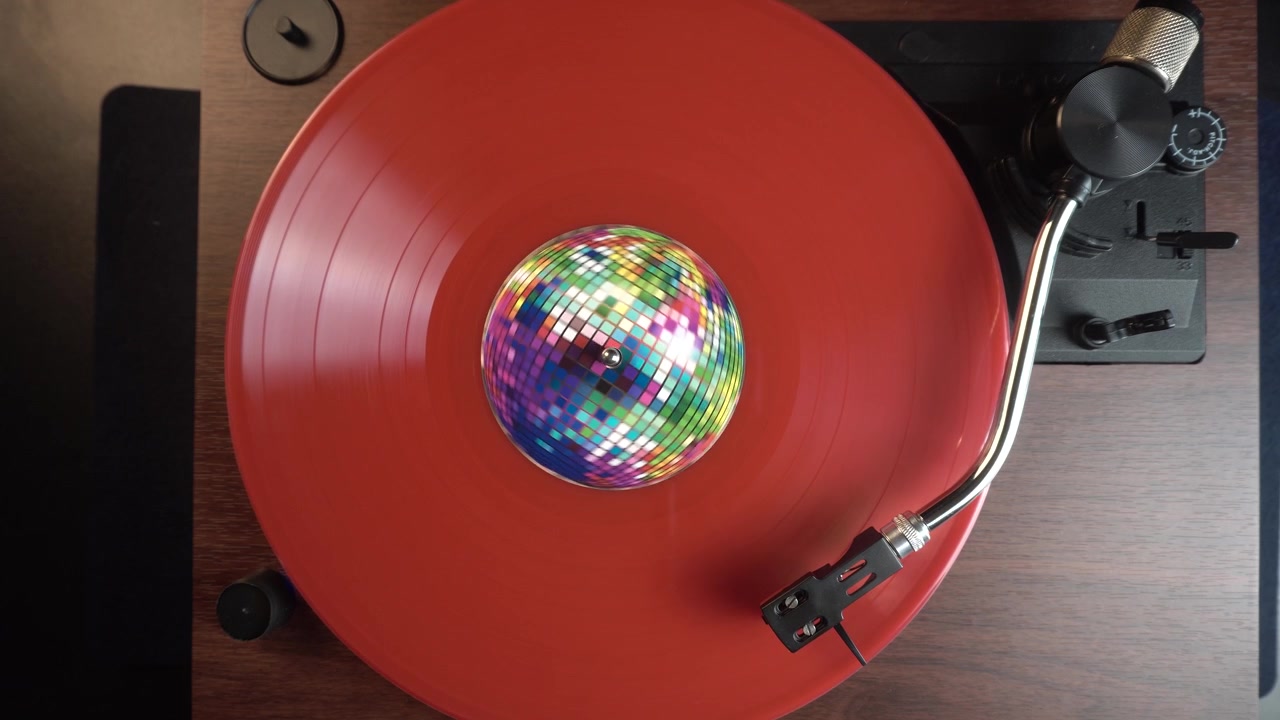 Riproduzione di un disco in vinile rosso con adesivo a palla da discoteca, collezione di musica vintage, vista dall'alto.
