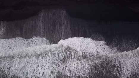 Mesmerizing-black-and-white-drone-aerial-of-powerful-waves-crashing-on-Vik's-black-sand-beach,-Iceland