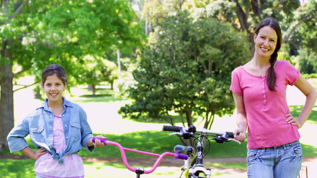 Madre e hija alegres paseando en bicicleta por el parque juntas
