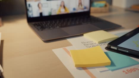 una mujer de negocios asiática que usa una computadora portátil habla con sus colegas sobre el plan en una reunión de videoconferencia en la sala de estar.