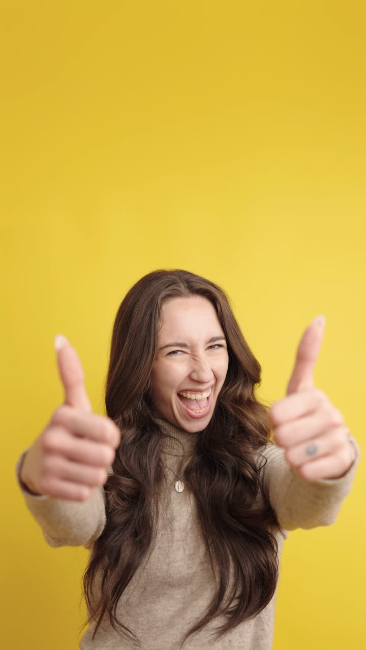 Woman giving thumbs up with excited expressions on yellow background