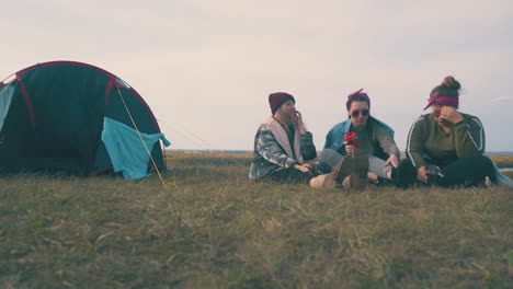 young women tourists drink alcohol by tent at sunset