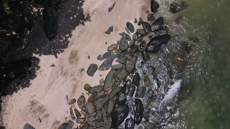 drone vertical tracking and tilt shot of jungle beach and rocky coastline with waves crashing on the shoreline