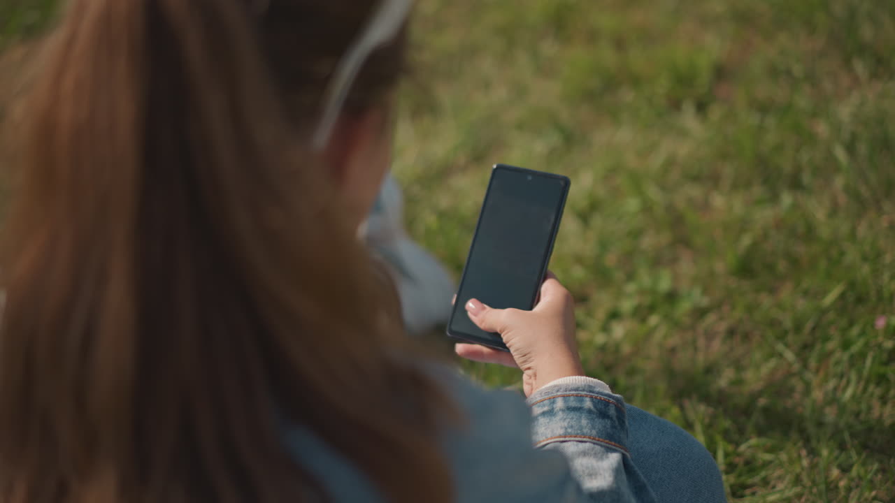 Giovane donna che si gode il riposo all'aperto. Adolescente che si rilassa comodamente all'esterno con il suo dispositivo elettronico. Giovane donna che si prende una pausa tranquilla all'aperto mentre è impegnata con il suo telefono cellulare.